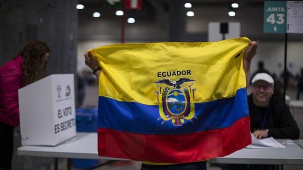 A woman holds an Ecuadorian flag at one of the voting tables